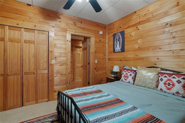 carpeted bedroom with ceiling fan, a paneled ceiling, a closet, and wood walls