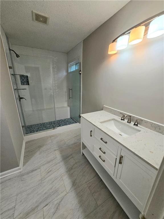 bathroom with vanity, a shower with shower door, and a textured ceiling