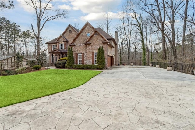 french country home featuring a front yard, a chimney, concrete driveway, a garage, and brick siding