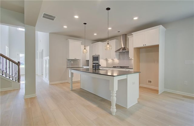 kitchen featuring decorative backsplash, dark countertops, light wood-style flooring, stainless steel appliances, and wall chimney range hood