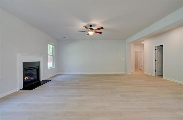 unfurnished living room featuring a ceiling fan, a glass covered fireplace, baseboards, and light wood finished floors