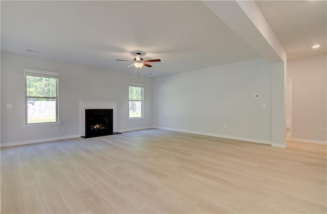 unfurnished living room featuring baseboards, a lit fireplace, light wood finished floors, and a healthy amount of sunlight