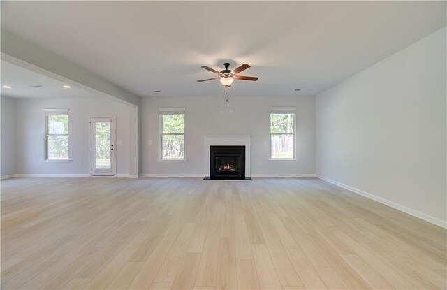 unfurnished living room with a fireplace with flush hearth, light wood-type flooring, baseboards, and a ceiling fan