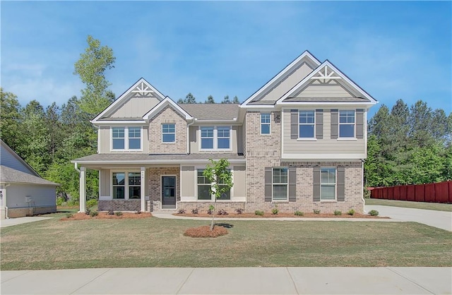 craftsman house with brick siding, fence, and a front lawn