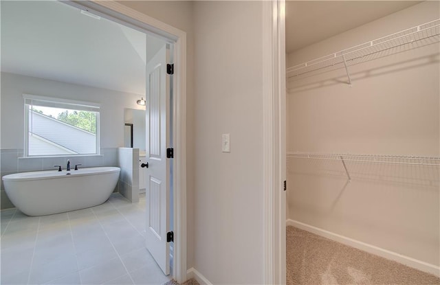 full bath featuring a freestanding tub, a spacious closet, baseboards, and tile patterned floors