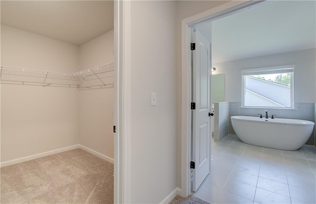 bathroom featuring a walk in closet, a soaking tub, baseboards, and tile patterned floors