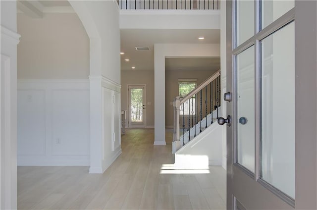 foyer with visible vents, a decorative wall, light wood-style floors, wainscoting, and stairs