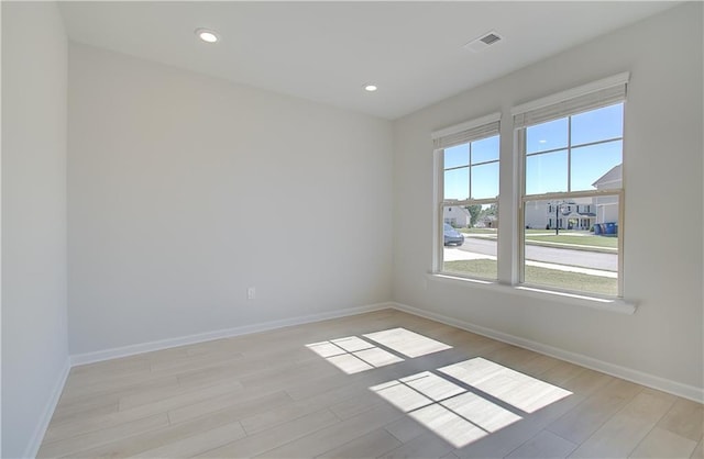 spare room featuring light wood-type flooring, visible vents, and baseboards