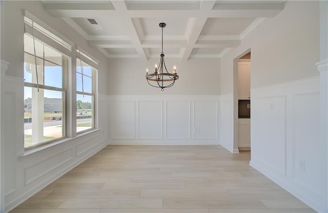 unfurnished dining area featuring a chandelier, a decorative wall, light wood-style flooring, and beamed ceiling