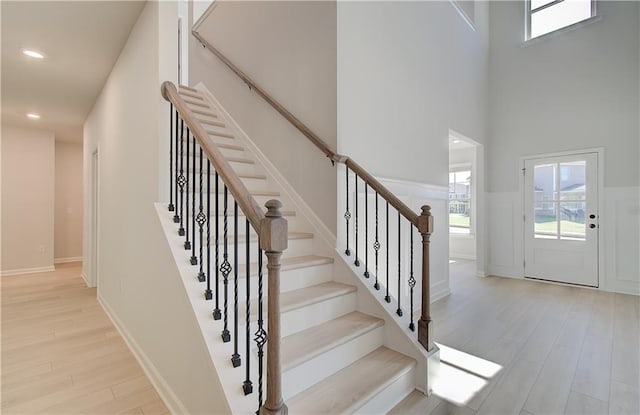 staircase featuring baseboards, wood finished floors, a towering ceiling, and recessed lighting