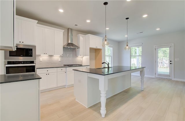 kitchen featuring a sink, appliances with stainless steel finishes, decorative backsplash, wall chimney exhaust hood, and dark countertops