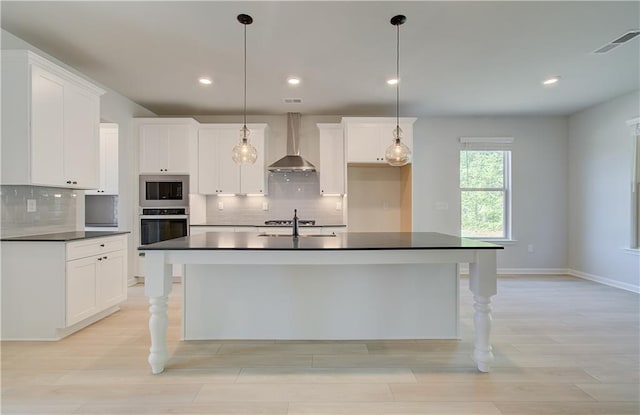 kitchen featuring visible vents, dark countertops, appliances with stainless steel finishes, wall chimney range hood, and a sink