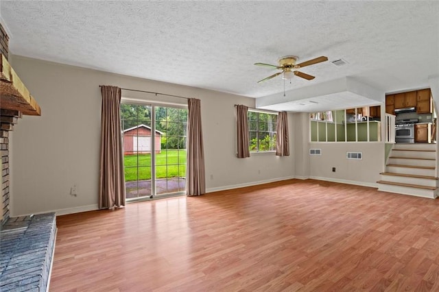 140 Carriage Cir, Stockbridge, GA 30281 - unfurnished living room with light wood finished floors, a ceiling fan, a textured ceiling, a brick fireplace, and stairway