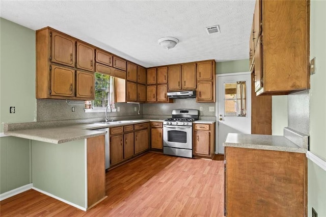 140 Carriage Cir, Stockbridge, GA 30281 - kitchen with appliances with stainless steel finishes, under cabinet range hood, light wood-style floors, brown cabinets, and a peninsula