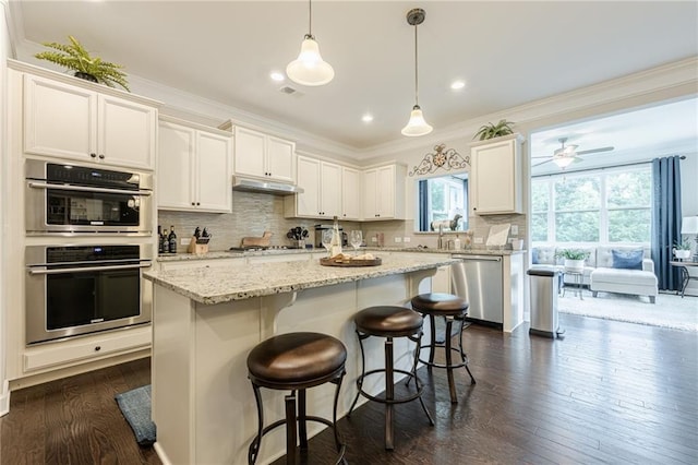 5515 Cheatam Ave, Cumming, GA 30040 - kitchen with appliances with stainless steel finishes, dark wood-style flooring, decorative backsplash, a kitchen breakfast bar, and white cabinets