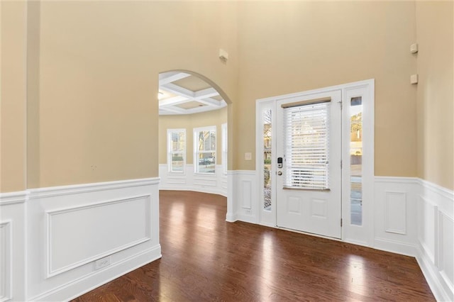 entrance foyer with beam ceiling, coffered ceiling, arched walkways, and wood finished floors