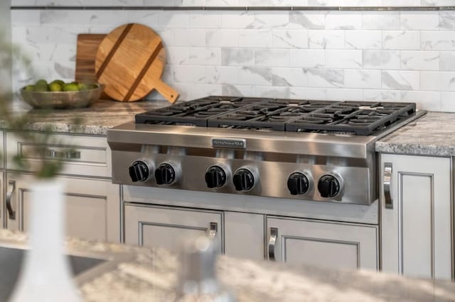 room details with stainless steel gas cooktop, light stone counters, and decorative backsplash