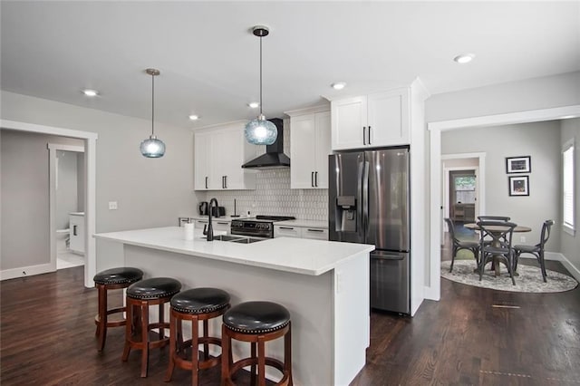 kitchen with appliances with stainless steel finishes, pendant lighting, white cabinets, a center island with sink, and wall chimney exhaust hood