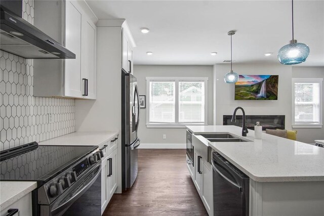 kitchen featuring white cabinetry, stainless steel appliances, light stone counters, decorative light fixtures, and wall chimney exhaust hood