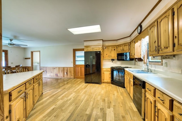 kitchen featuring ceiling fan, wood walls, black appliances, light hardwood / wood-style floors, and sink