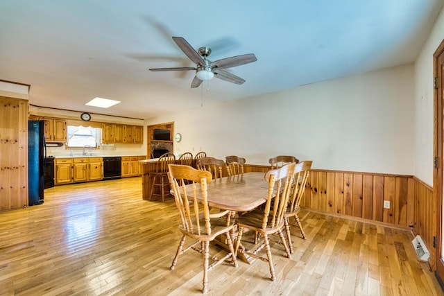 dining space with wood walls, a skylight, sink, light hardwood / wood-style floors, and ceiling fan