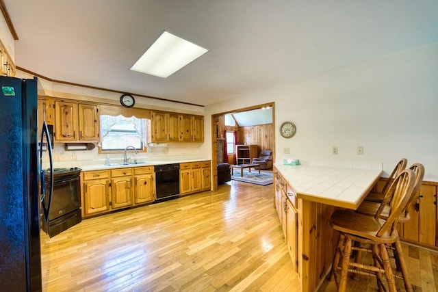 kitchen with sink, black appliances, a breakfast bar, light hardwood / wood-style floors, and a skylight