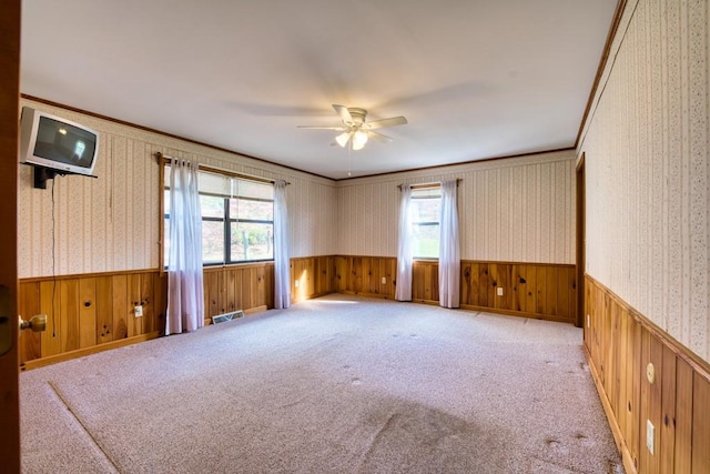 empty room with wood walls, light colored carpet, and ceiling fan