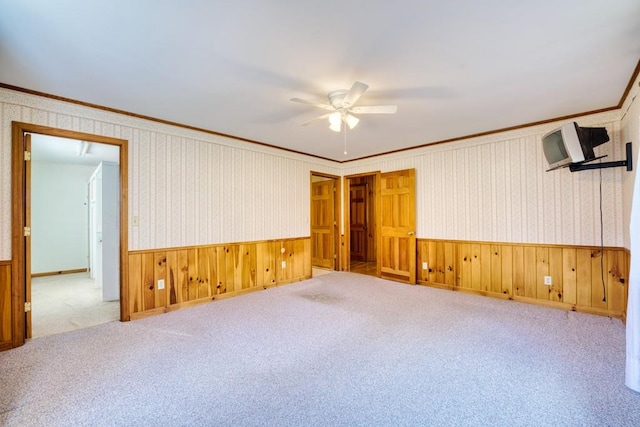 spare room featuring ceiling fan, light carpet, ornamental molding, and wood walls