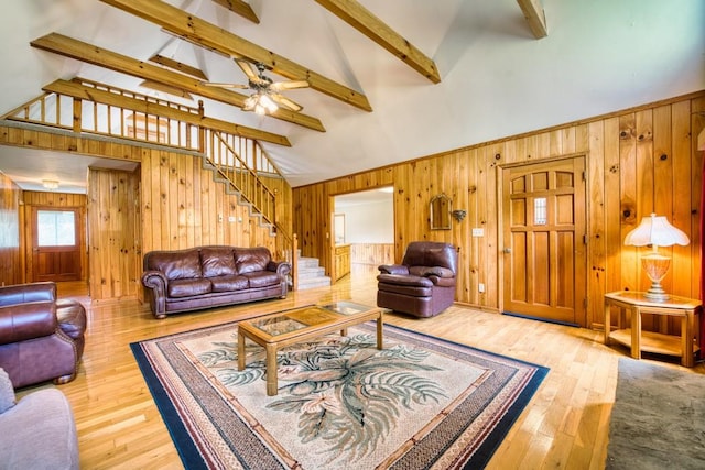 living room featuring hardwood / wood-style flooring, beamed ceiling, wooden walls, high vaulted ceiling, and ceiling fan