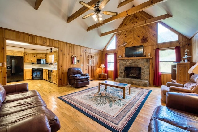 living room with beam ceiling, high vaulted ceiling, a stone fireplace, wood walls, and light hardwood / wood-style floors