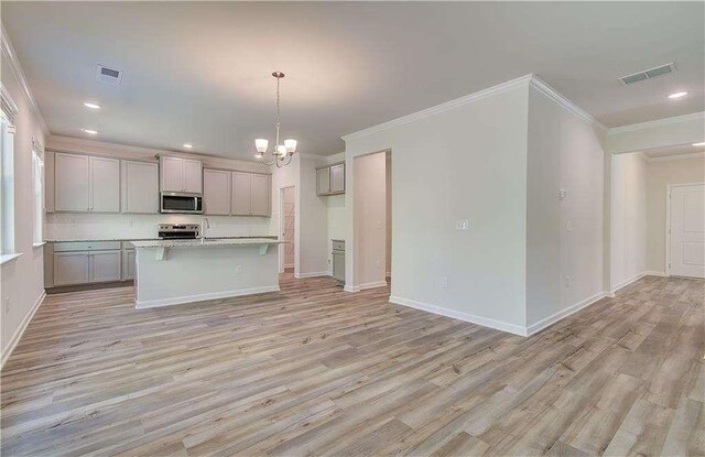 kitchen with gray cabinetry, light wood-type flooring, a center island with sink, appliances with stainless steel finishes, and ornamental molding