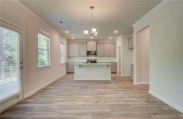 kitchen with gray cabinets, ornamental molding, an island with sink, decorative light fixtures, and light hardwood / wood-style floors