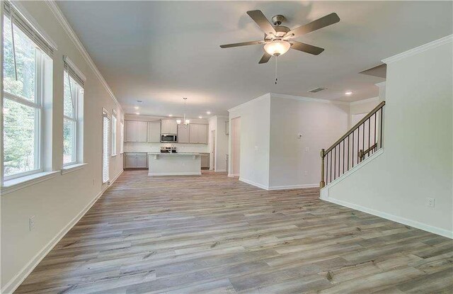 unfurnished living room featuring crown molding, light hardwood / wood-style flooring, and ceiling fan with notable chandelier