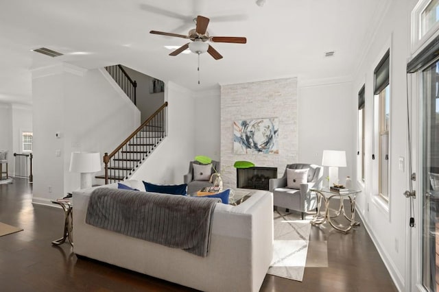 living room with visible vents, ornamental molding, wood finished floors, and a stone fireplace