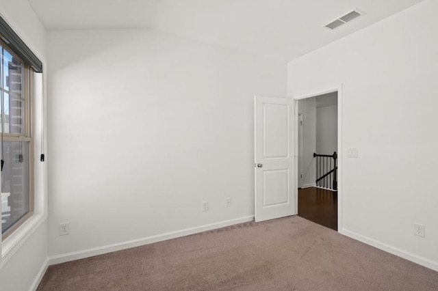 carpeted spare room featuring baseboards, visible vents, and vaulted ceiling