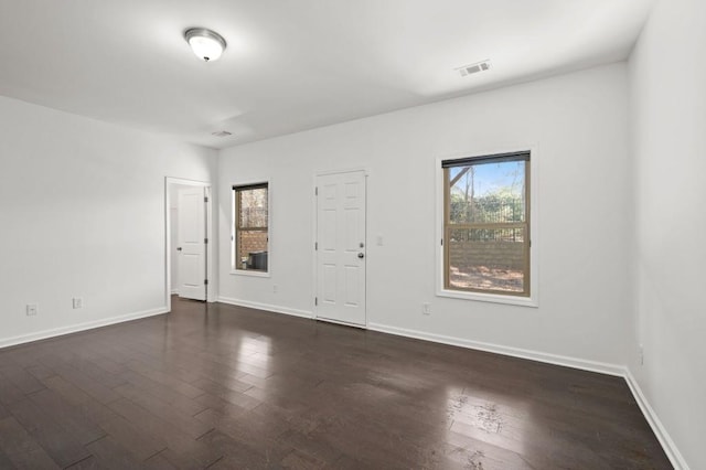 spare room with dark wood-style floors, visible vents, and baseboards