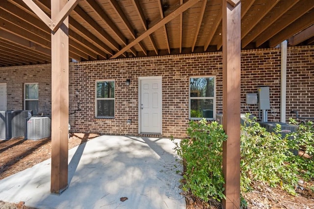 property entrance featuring central AC unit, a patio, and brick siding