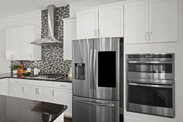 kitchen with white cabinetry, appliances with stainless steel finishes, wall chimney range hood, backsplash, and dark stone counters