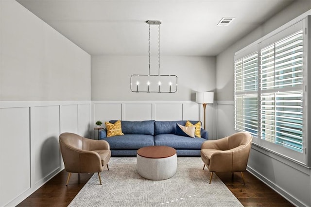 living area with a notable chandelier, visible vents, wood finished floors, and wainscoting