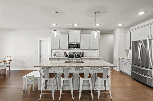 kitchen with light stone countertops, a kitchen island with sink, appliances with stainless steel finishes, and decorative light fixtures