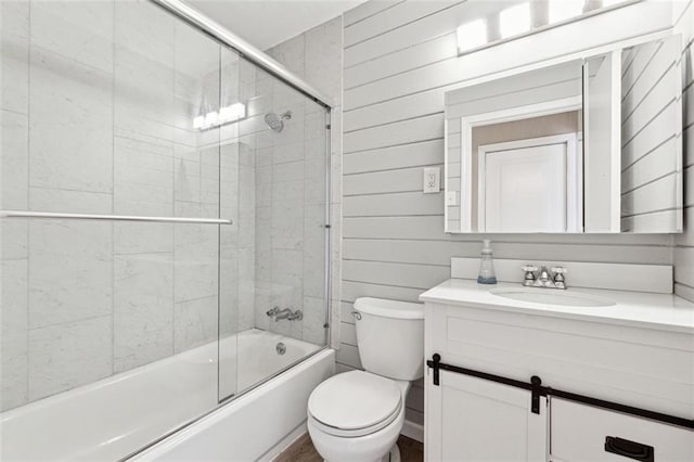 full bathroom featuring vanity, toilet, shower / bath combination with glass door, and wooden walls