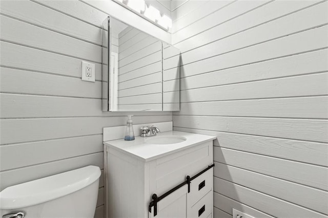 bathroom with vanity, toilet, and wood walls