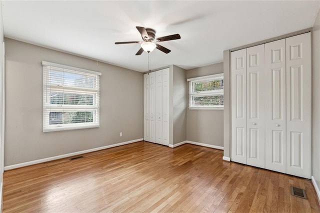 unfurnished bedroom with two closets, light hardwood / wood-style flooring, and ceiling fan