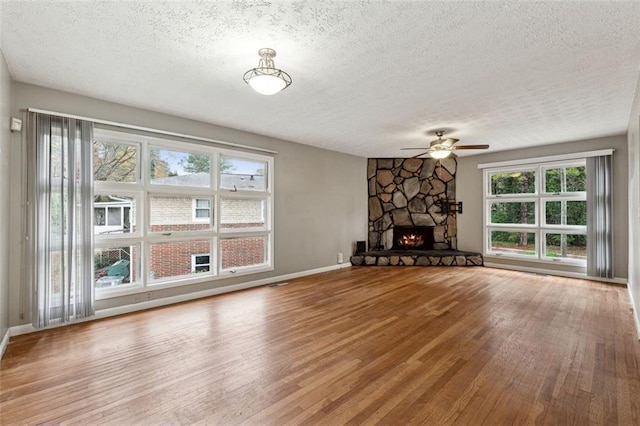 unfurnished living room with a stone fireplace, plenty of natural light, hardwood / wood-style floors, and a textured ceiling