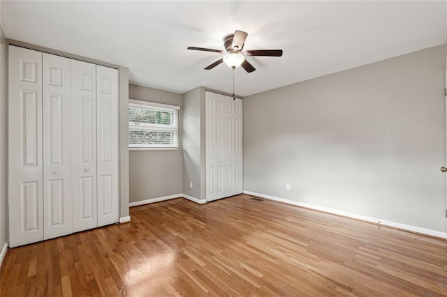 unfurnished bedroom with ceiling fan, multiple closets, and light hardwood / wood-style flooring