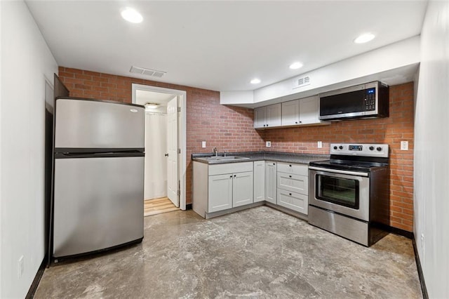 kitchen with brick wall, white cabinetry, sink, and appliances with stainless steel finishes