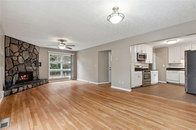 unfurnished living room with a fireplace, light hardwood / wood-style floors, a textured ceiling, and ceiling fan