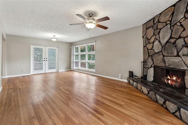 unfurnished living room with french doors, ceiling fan, a fireplace, a textured ceiling, and light hardwood / wood-style floors