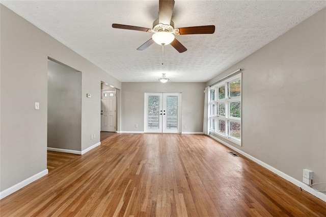 empty room with french doors, ceiling fan, light hardwood / wood-style flooring, and a textured ceiling