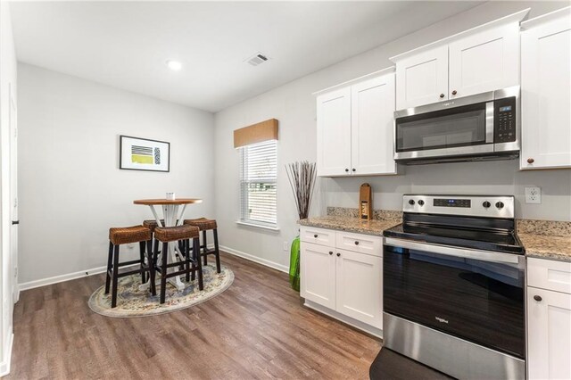 kitchen with wood-type flooring, light stone counters, stainless steel appliances, and white cabinets